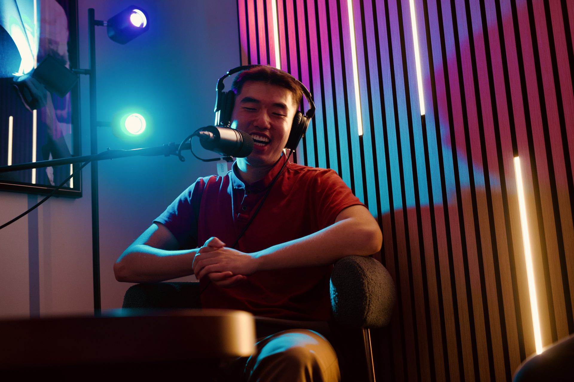 Host laughing at the microphone under colorful LED lighting in the podcast room