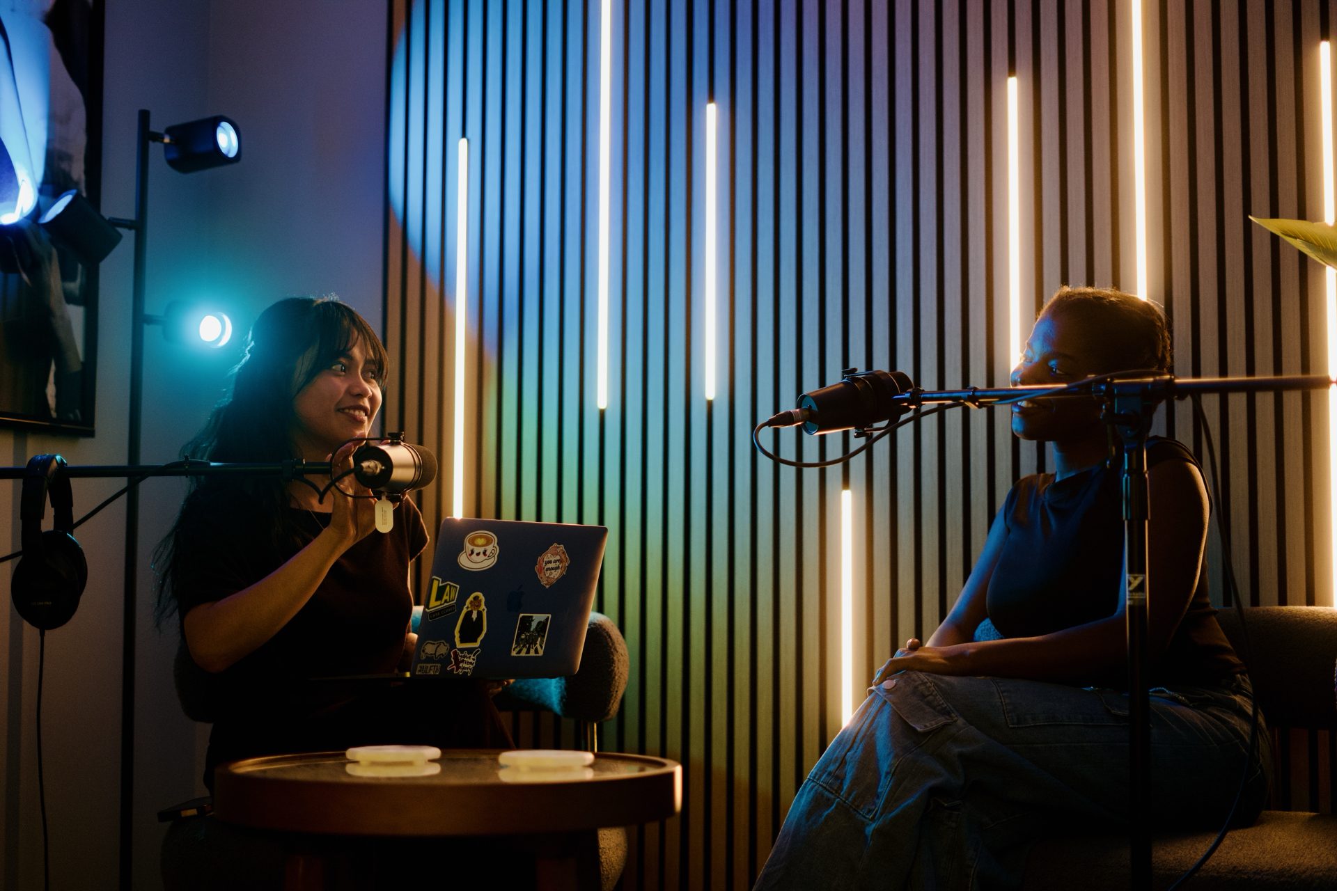 Two hosts recording in the podcast room with microphones and a wood slat accent wall